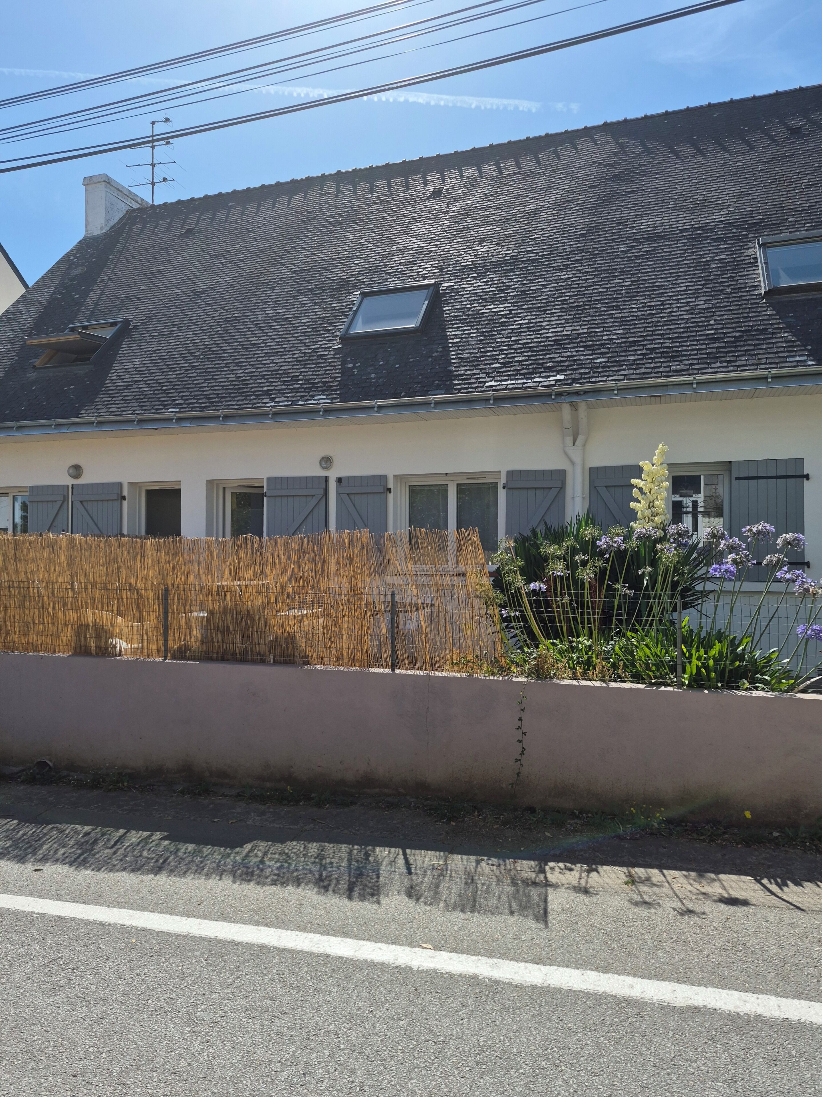 Ein Wohngebäude mit geneigtem Dach, einem kleinen Fenster und einer Bepflanzung an der Zäunung.