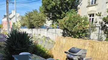 An outdoor patio with a glass table and white plastic chairs, surrounded by a bamboo fence and various plants.