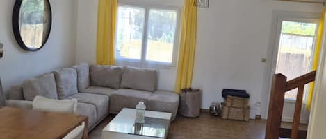 A living room with a sofa, a coffee table, a dining table, and a window with curtains.