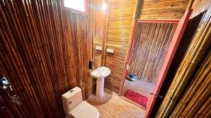Un baño con inodoro, lavamanos y un cubo rojo en el suelo.