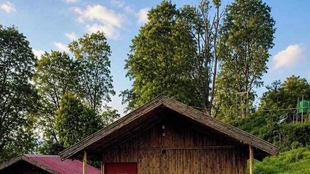 Una cabaña de madera rústica con puerta roja, un balcón y unos pocos escalones que llevan a la entrada.