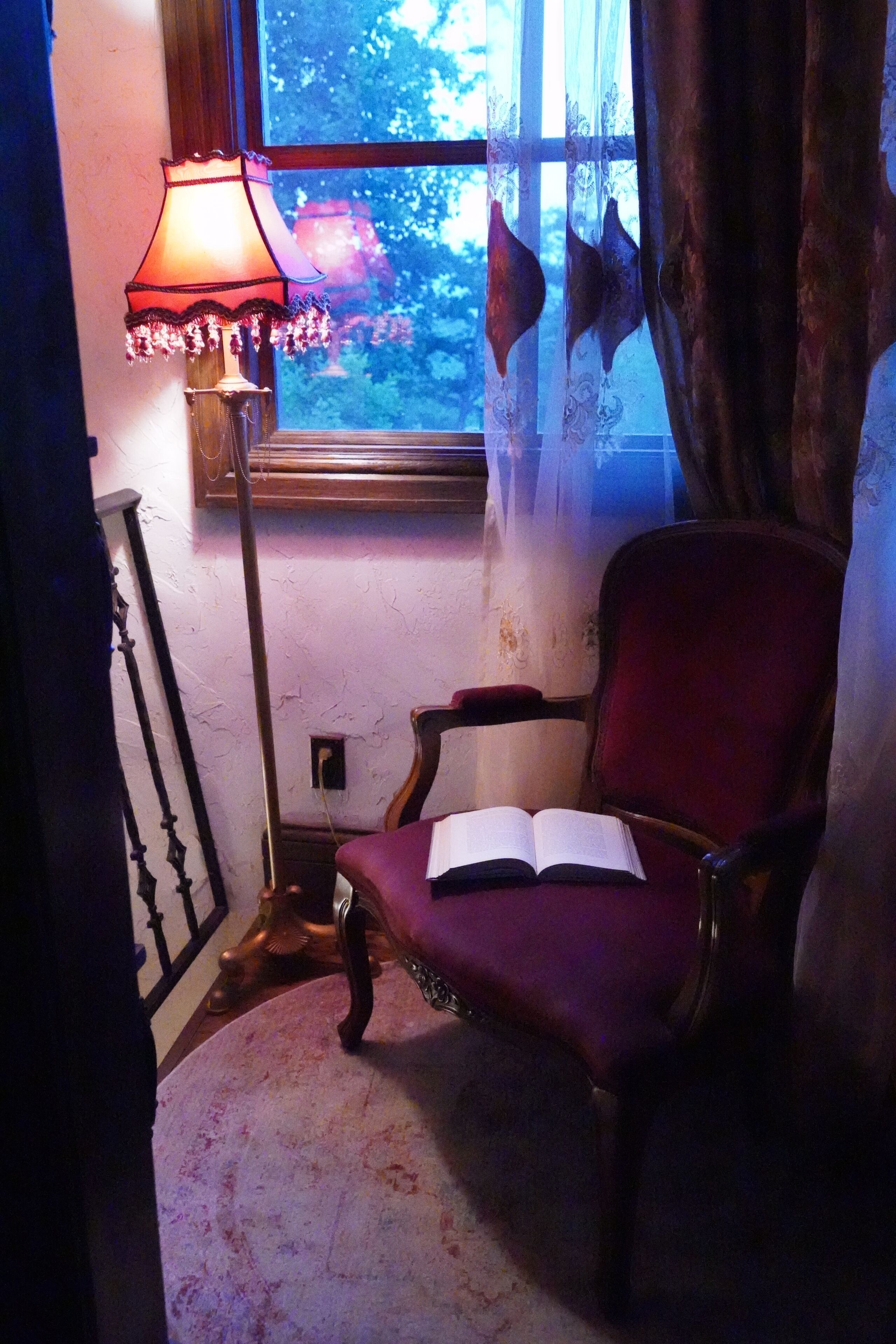 A room with a red armchair, a floor lamp, and a window with curtains.