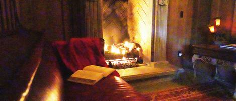 Una sala acogedora con chimenea, un sofá de cuero rojo y un libro sobre la mesa.