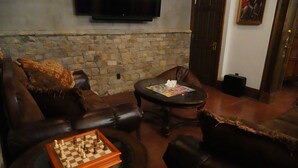 A living room with a stone wall, leather sofas, a coffee table with a chessboard, and a television mounted above. - Family friendly castle, 17th century archaic chateau, providing all amenities. (Franklin)