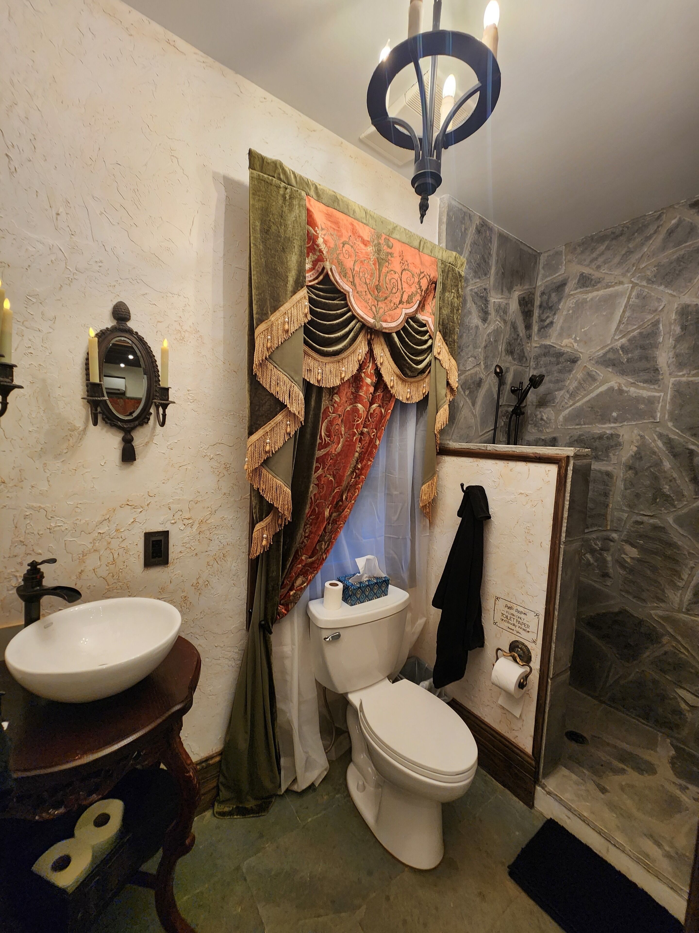 Un baño con lavamanos blanco, inodoro, ducha con pared de piedra y candelabro.