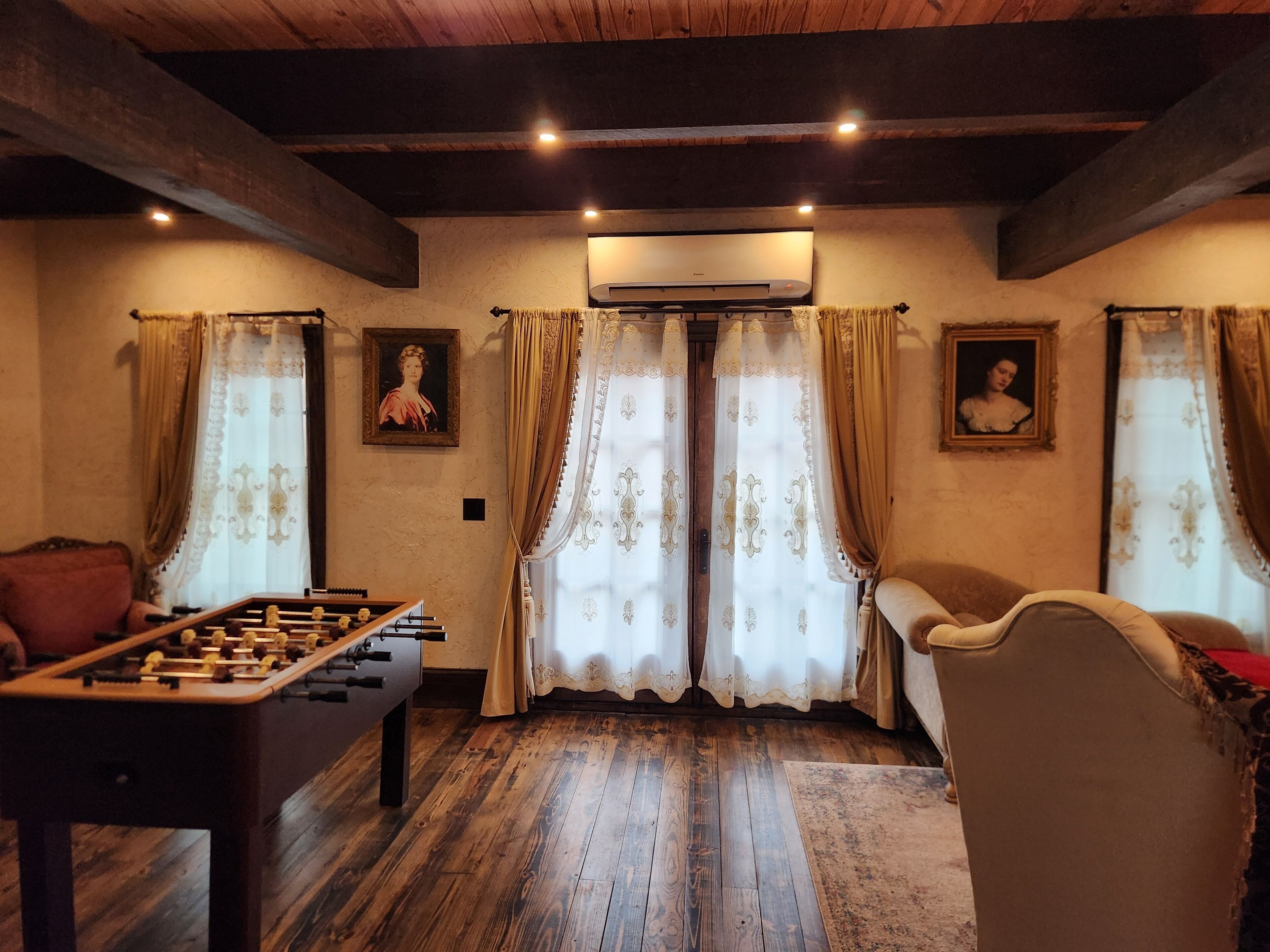 A room with a foosball table, two framed portraits, and a ceiling fan.
