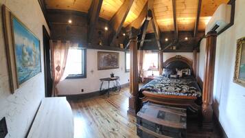 A room with a wooden ceiling, a bed with a patterned bedspread, a small table, and a painting on the wall.