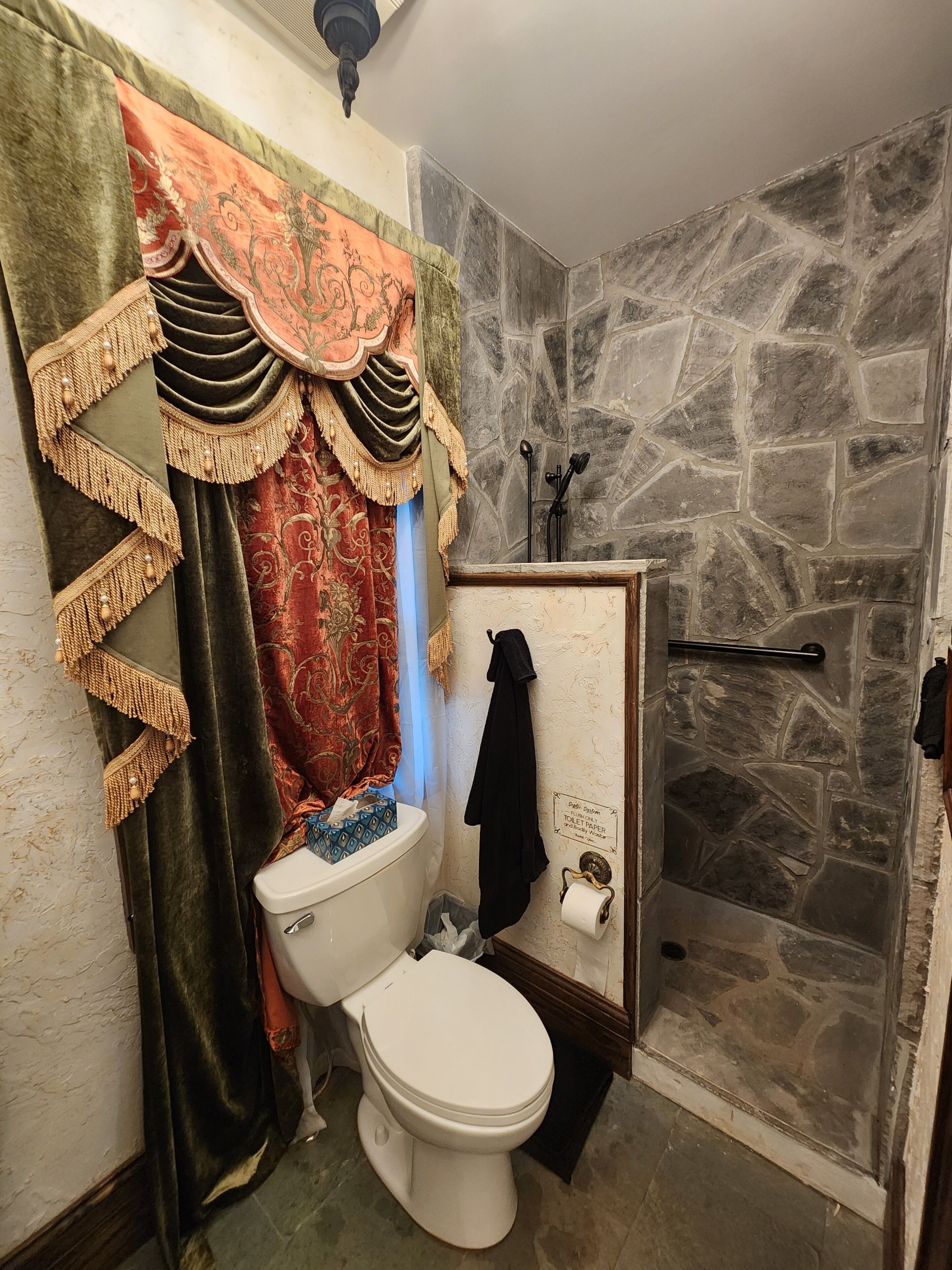 A bathroom with a stone wall, a toilet, a shower, and a towel rack.