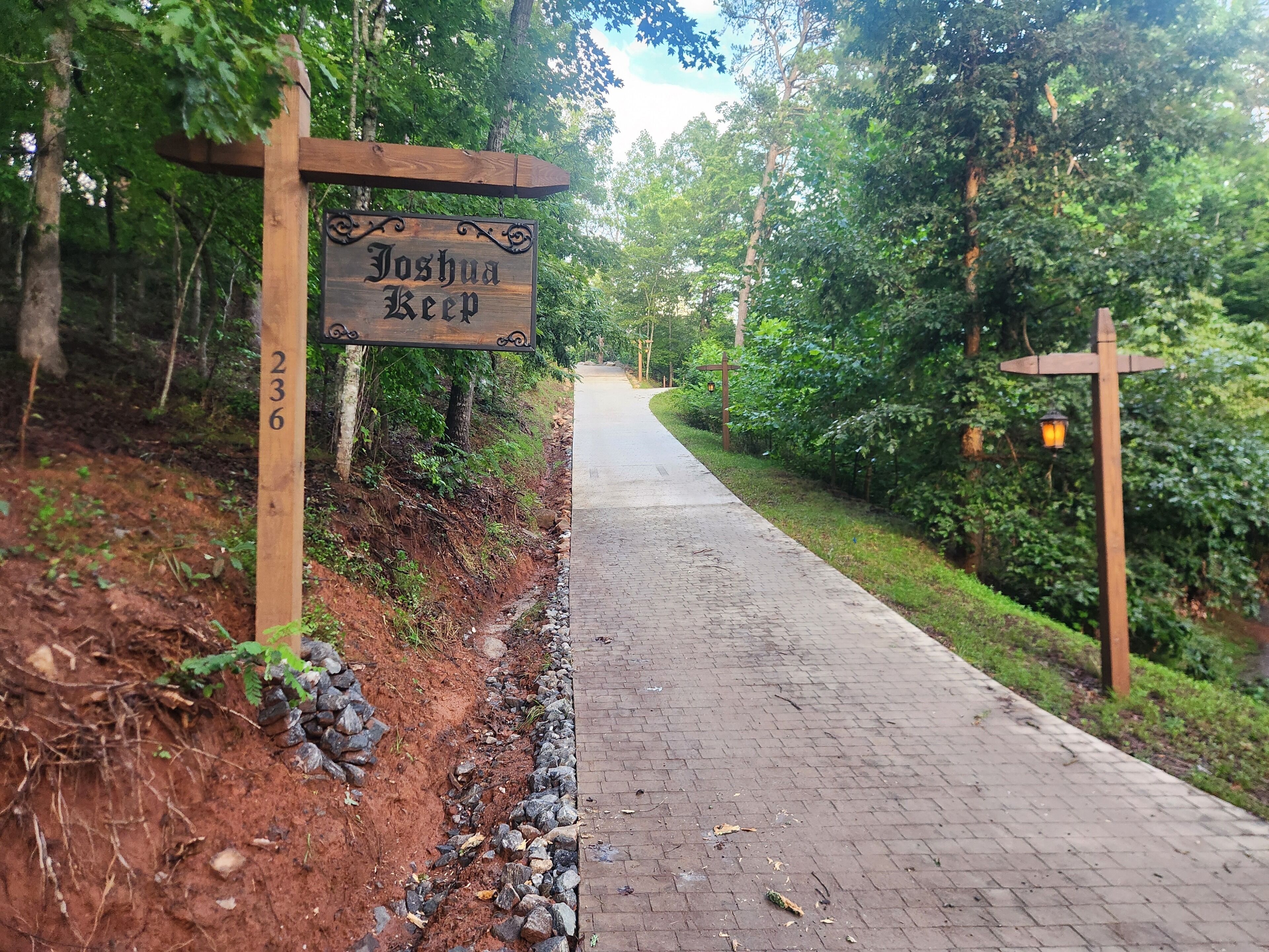 A pathway with a wooden sign reading 'Joshua Keep 236' surrounded by greenery.