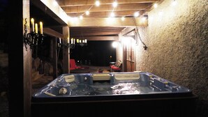 A hot tub under a wooden pergola with string lights, surrounded by stone walls and a red chair. - Family friendly castle, 17th century archaic chateau, providing all amenities. (Franklin)