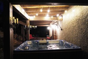 A hot tub under a wooden pergola with string lights, surrounded by stone walls and a red chair. - Family friendly castle, 17th century archaic chateau, providing all amenities. (Franklin)