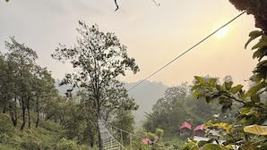 A rope bridge in a lush, green forest with a clear sky. - The Ameya mountain view bamboo cottages (Kanda Khal)