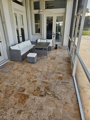 Ein überdachter Patio-Bereich mit einer Sitzecke, bestehend aus einer Couch und einem Tisch, einem Deckenventilator und Blick durch Glastüren.