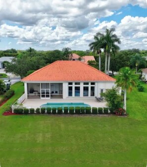A single-story house with a red-tiled roof, a covered patio, and a well-maintained lawn. - Lakefront home with priv heated pool & priv gym. Enclosed patio with grill. (Palm City)