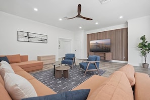 A modern living room with a sofa, chairs, a coffee table, a TV, and a ceiling fan. - The Showstopper Luxury Home - Indian Trails (Palm Harbor)