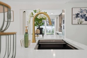 A modern kitchen with a gold faucet, a green bottle, and a potted plant. - The Showstopper Luxury Home - Indian Trails (Palm Harbor)