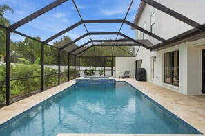 A swimming pool with a glass enclosure, surrounded by a house with a white exterior and large windows. - The Showstopper Luxury Home - Indian Trails (Palm Harbor)