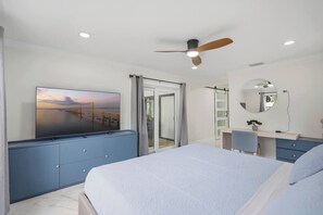 A modern bedroom with a bed, a TV, a ceiling fan, and a bathroom with a shower and toilet. - The Showstopper Luxury Home - Indian Trails (Palm Harbor)