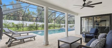 Un espacio al aire libre techado con piscina, sillas de descanso, una mesa y una zona de estar.