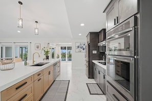 A modern kitchen with stainless steel appliances, a white countertop, and a view to the outside. - The Showstopper Luxury Home - Indian Trails (Palm Harbor)