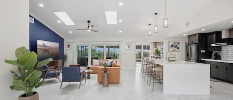 A spacious living area with a large TV, comfortable seating, a kitchen with modern appliances, and a view of the outdoors.