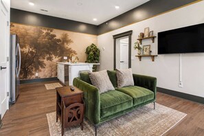 A modern living room with a green sofa, a small wooden side table, and a large wall-mounted TV. - The Bavarian Inn 2 1BDR Stay (Covington)