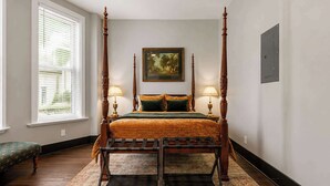 Una cama con dosel de madera, con un edredón verde y dos lámparas a cada lado.