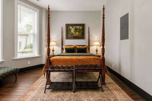 Ein Bett mit Baldachin, dessen Gestell aus Holz ist, mit einem grünen Überwurf und je einer Lampe auf jeder Seite.