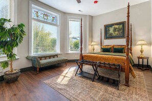 A four-poster bed with a wooden frame and a green bedspread, a bench with a patterned cushion, and a potted plant. - The Bavarian Inn 2 1BDR Stay (Covington)