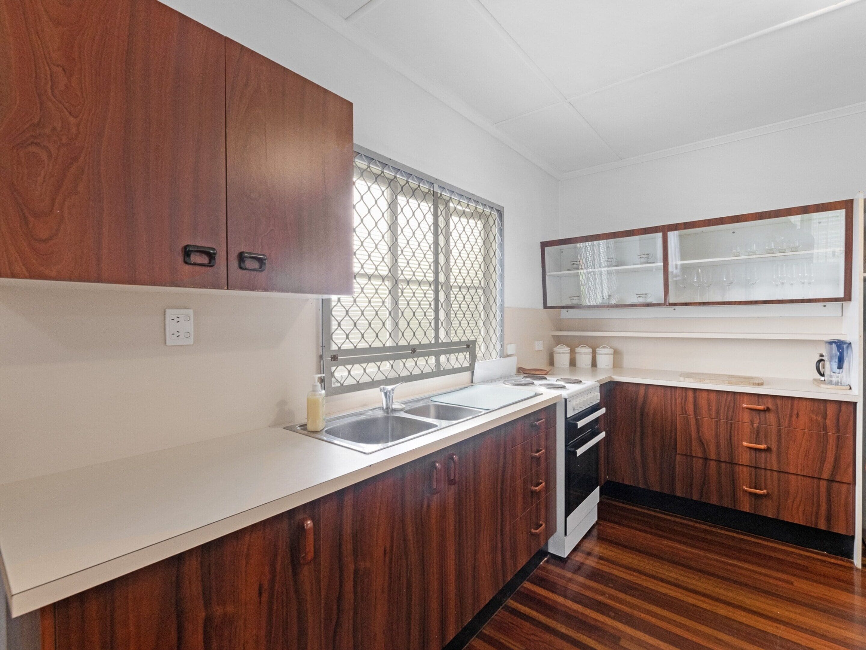 A kitchen with wooden cabinets, a white countertop, a window with a metal screen, and a stove.