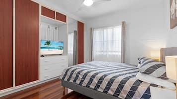 A bedroom with a bed, a television on a dresser, and a ceiling fan.
