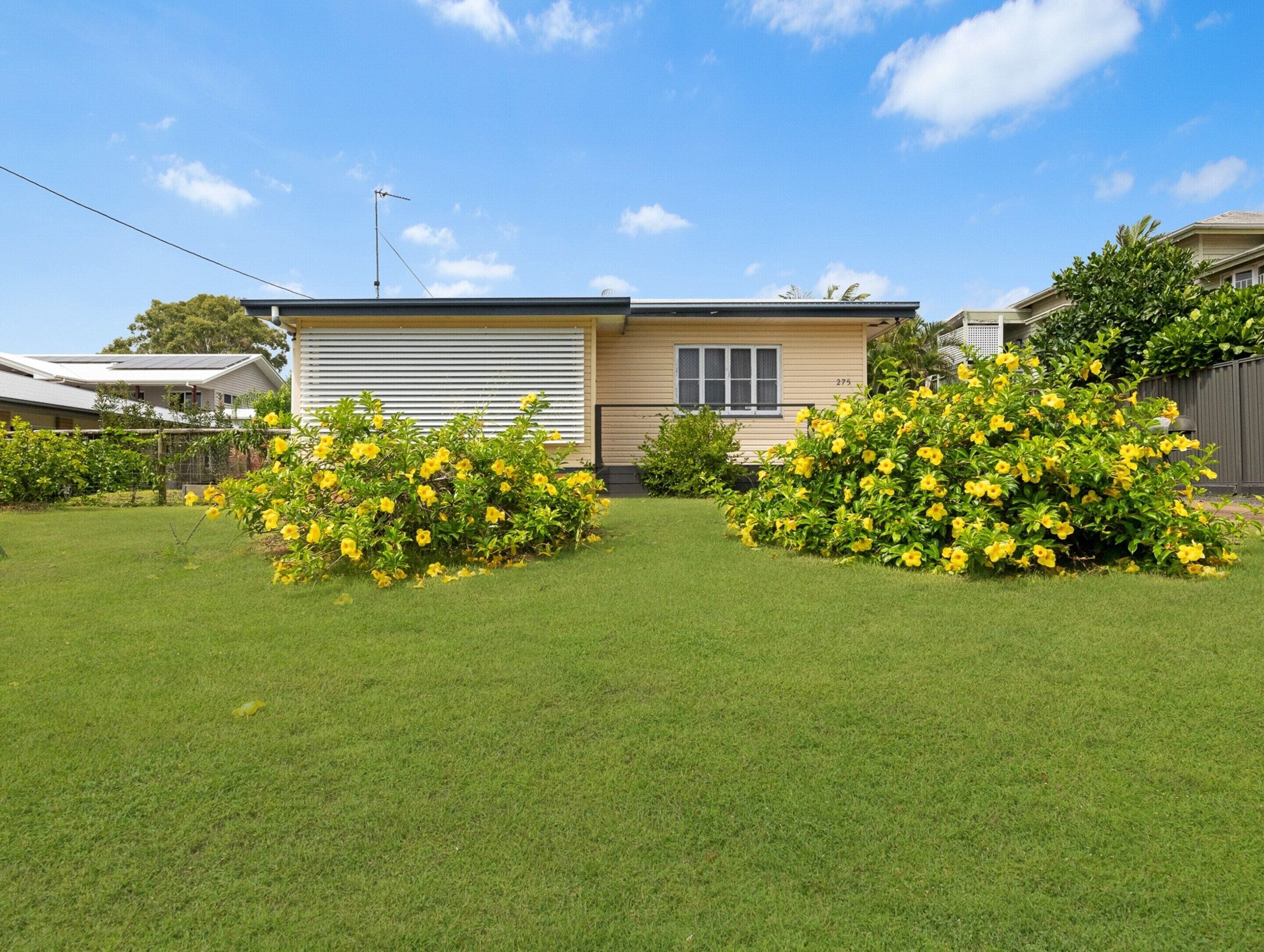 A single-story house with a garage, surrounded by well-maintained grass and yellow flowering bushes.