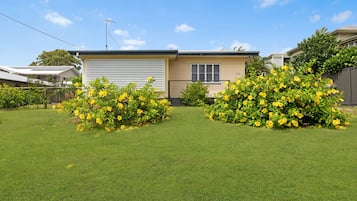 A single-story house with a garage, surrounded by well-maintained grass and yellow flowering bushes.