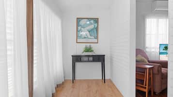 A hallway with a wooden floor, white walls, a black console table with a plant, and a framed artwork on the wall.