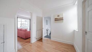 A hallway with a wooden floor, a red sofa in the background, a radiator, and a wall-mounted artwork.