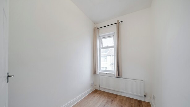 A room with a single window, white walls, and wooden flooring.