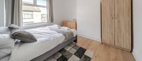 A bedroom with a bed, a wooden wardrobe, a radiator, and a window with curtains.