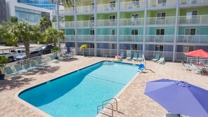 A swimming pool with lounge chairs and umbrellas, surrounded by a multi-story building with balconies. - Pelican Pointe 425:Walk to Beach~Pool~Free Parking (Clearwater Beach)