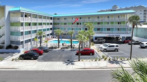 A multi-story hotel with a swimming pool, parking area, and a sign reading 'PELICAN POINT'. - Pelican Pointe 425:Walk to Beach~Pool~Free Parking (Clearwater Beach)