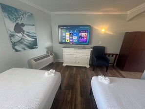 A hotel room with two beds, a television displaying a home screen, a wall-mounted air conditioner, and a large poster. - Pelican Pointe 425:Walk to Beach~Pool~Free Parking (Clearwater Beach)