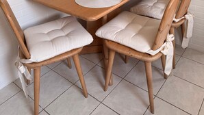 A dining area with a wooden table, four cushioned chairs, a white pendant light, and a kitchen in the background. - Rosmarie Vacation Rental—in the Heart of Rheinhessen (Alzey)