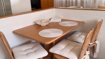 Ein Essbereich mit einem Holztisch, vier gepolsterten Stühlen, einer weißen Pendelleuchte und einer Küche im Hintergrund.