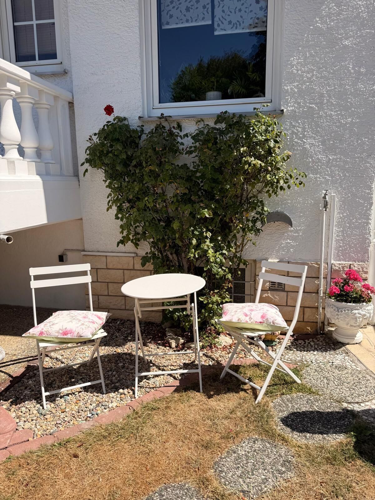 Eine Terrasse mit zwei weißen Stühlen und einem kleinen Tisch, umgeben von Kieselsteinen und einem Blumentopf.
