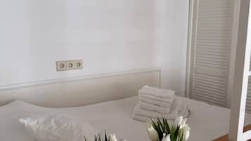 Une chambre à coucher avec un lit, des oreillers blancs, une table de chevet en bois et deux vases en verre contenant des fleurs blanches.