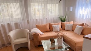 A living room with a sofa, a chair, a glass coffee table, and sheer curtains. - Rosmarie Vacation Rental—in the Heart of Rheinhessen (Alzey)