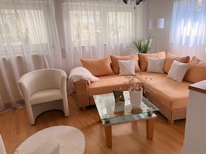 A living room with a sofa, a chair, a glass coffee table, and sheer curtains. - Rosmarie Vacation Rental—in the Heart of Rheinhessen (Alzey)