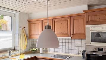 Une cuisine avec des meubles en bois, un plafond blanc, un luminaire suspendu, un four à micro-ondes et un lave-vaisselle.