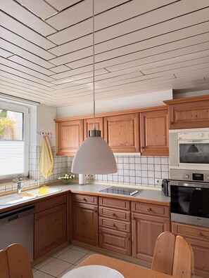 A kitchen with wooden cabinets, a white ceiling, a hanging pendant light, a microwave, and a dishwasher. - Rosmarie Vacation Rental—in the Heart of Rheinhessen (Alzey)
