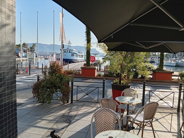 An outdoor seating area with wicker chairs and tables, a view of the marina with boats, and a clear sky.