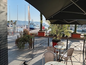 An outdoor seating area with wicker chairs and tables, a view of the marina with boats, and a clear sky.